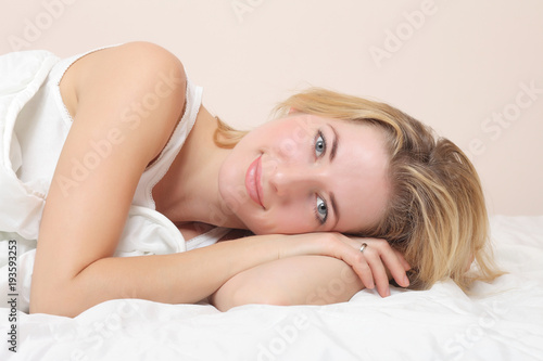 Smiling lady lies in bed indoors.