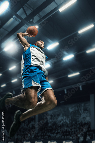 Basketball player on big professional arena during the game. Basketball player making slam dunk.