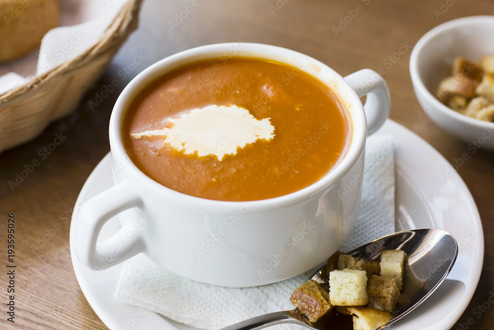 Tomato puree soup with cream and crackers in a white plate on the table Tomato puree soup with cream and crackers in a white plate on the table