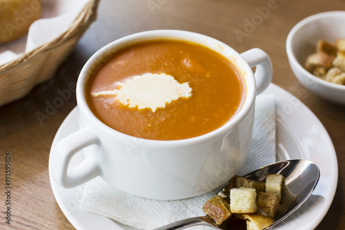 Tomato puree soup with cream and crackers in a white plate on the table