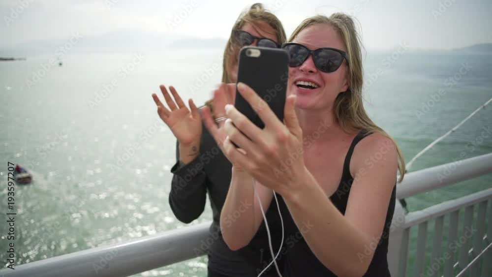 Lesbian couple talking by video on phone on bridge at sunset rapid slow motion