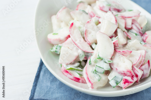 Healthy Red Radish and Green Scallion Onions Salad with Greek Yogurt Dressing in White Serving Bowl Standing on Blue Napkin. Easter Brunch Meal Spring Menu.