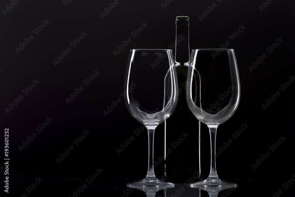 two wine glasses and bottle of wine behind said glasses on black background two wine glasses and bottle of wine behind said glasses on black background
