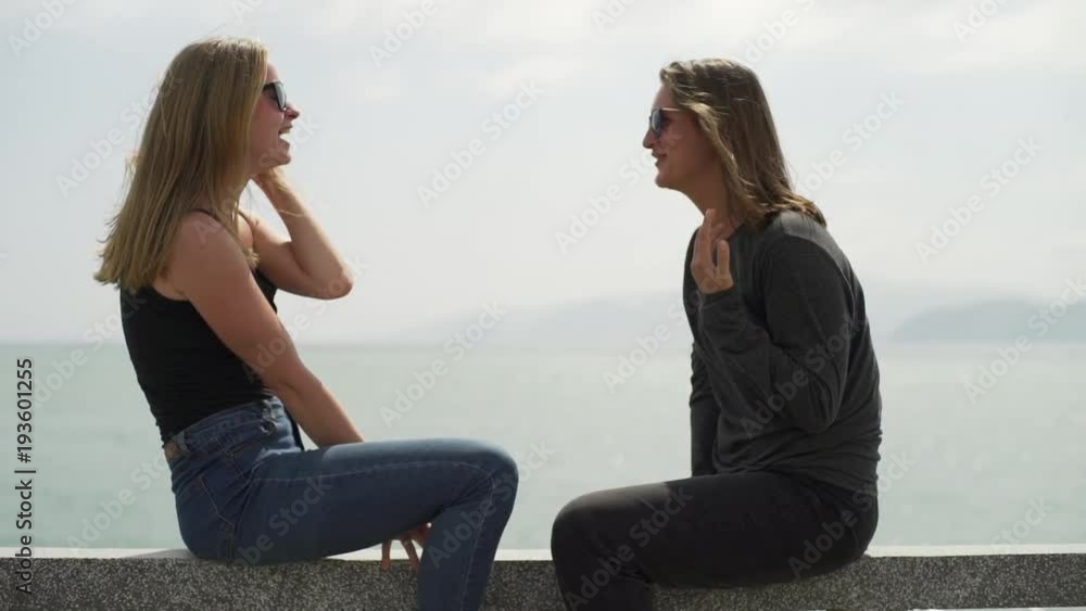 Lesbian couple sit on the bridge,talk and laugh at sunset rapid slow motion Lesbian couple sit on the bridge,talk and laugh at sunset rapid slow motion