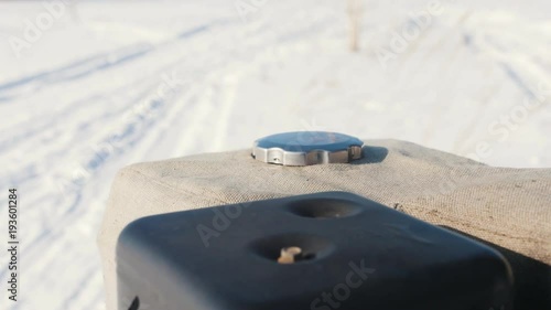 Man tightening the gas cap of a mini snowmobile on a winter snowy road photo