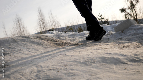 Close-up of male legs in winter shoes walking on snow. View of walking on snow with Snow shoes and Shoe spikes in winter. Men's legs in boots close up the snow-covered path photo