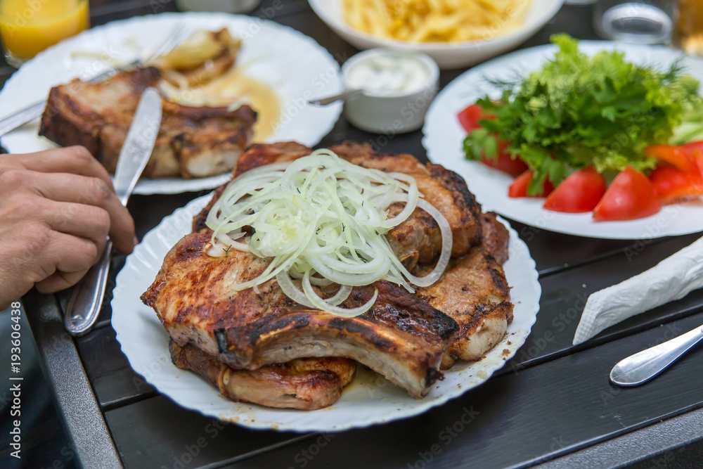 Fried pork steaks, cutlets with bones with onions, on a wooden table. A man's hand holds a knife Fried pork steaks, cutlets with bones with onions, on a wooden table. A man's hand holds a knife