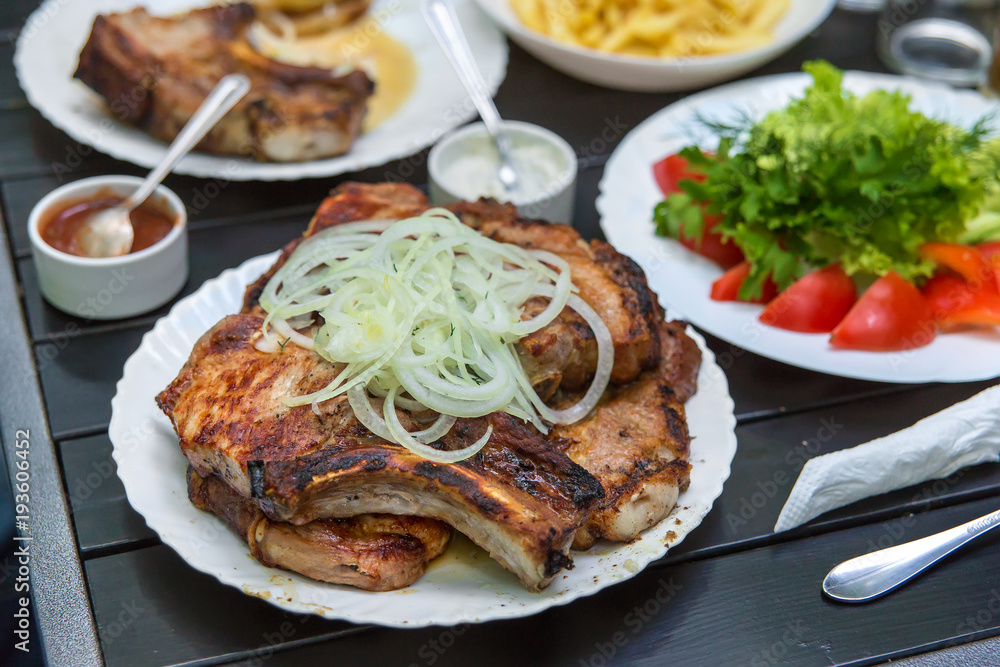 Fried pork steaks, cutlets with bones with onions, on a wooden table. A man's hand holds a knife Fried pork steaks, cutlets with bones with onions, on a wooden table. A man's hand holds a knife
