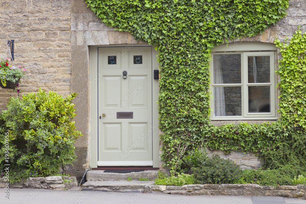 Wooden doors to a charming lime stone cottage surrounded by climbing ivy plant and shrubs .