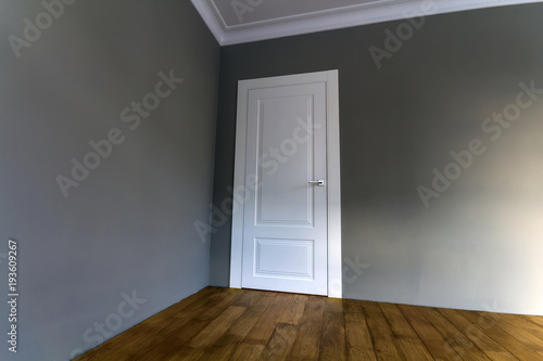 New renovated room interior with freshly painted walls  white door and wooden parquet floor