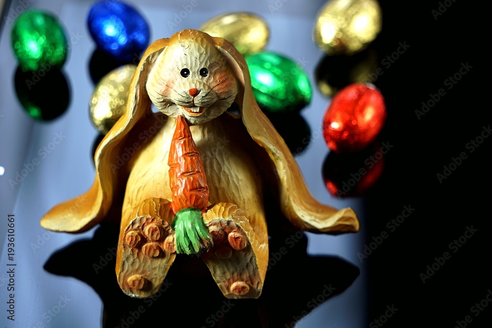 a smiling bunny  with a carrot on a mirror surface with chocolate sweets. chocolate eggs
