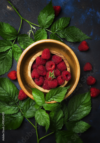 Fresh raspberries and green leaves in wooden bowl, top view