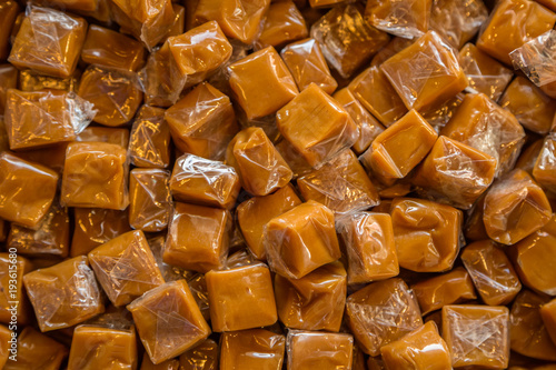 Fotografie Toffee candy brown background. Caramel cubes close up