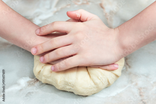 Children hands knead the dough on the table, closeup