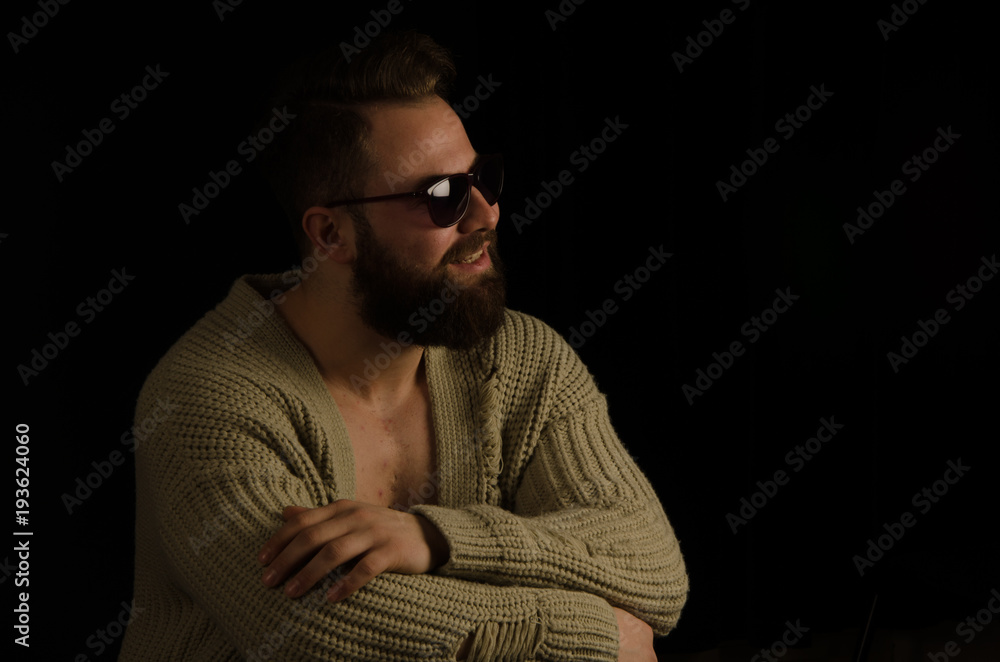 The young model posing in the studio is dressed in a cardigan and has bearded in his pockets and bearded .. sitting on a chair, looking forward and happy The young model posing in the studio is dressed in a cardigan and has bearded in his pockets and bearded .. sitting on a chair, looking forward and happy