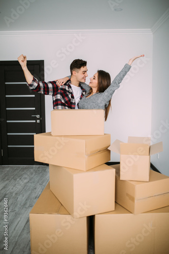 cheerful and happy young couple victory raised hands of their new home with moving cardboard box during move into new apartment