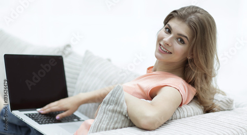 beautiful young woman working with laptop sitting on sofa and looking at camera.
