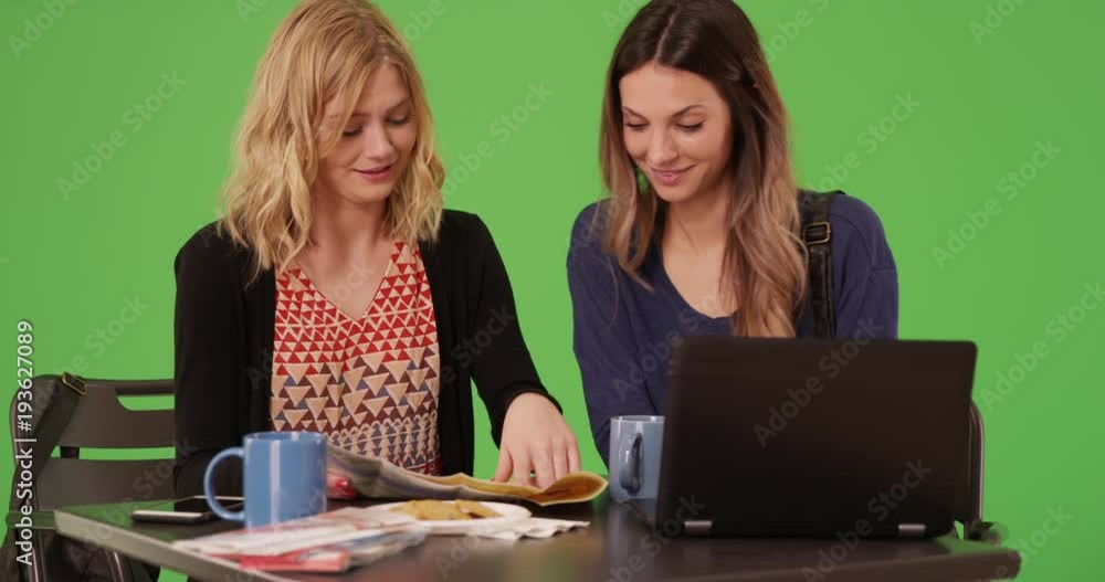 Two beautiful tourist girls looking at travel maps and laptop on green screen Two beautiful tourist girls looking at travel maps and laptop on green screen