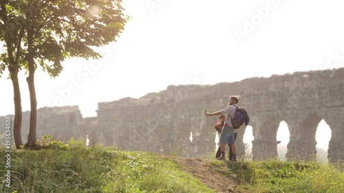 Young lovely couple backpackers tourists taking selfies photo on hill in front of roman aqueduct arches in parco degli acquedotti park ruins in rome on romantic misty sunrise with sleeping bag slow photo