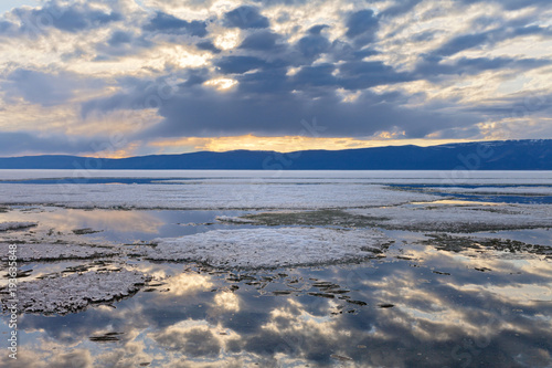 Lake Baikal on a spring evening. The ice melts in the bay near the island of Olkhon. The overcast sky is reflected in the water