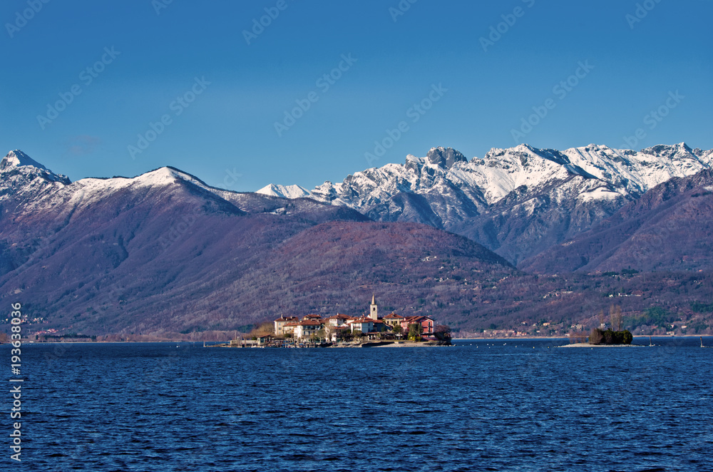a sunny winter day with the tops of the mountains covered with snow, the lMaggiore Lake and the island Pescatori