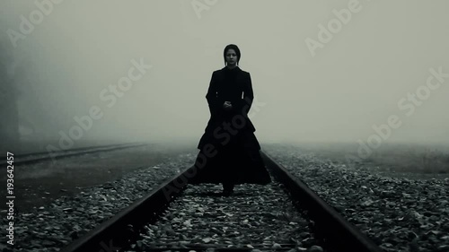 Horror scene of a terrifying woman in black dress staying at trails in the fog photo