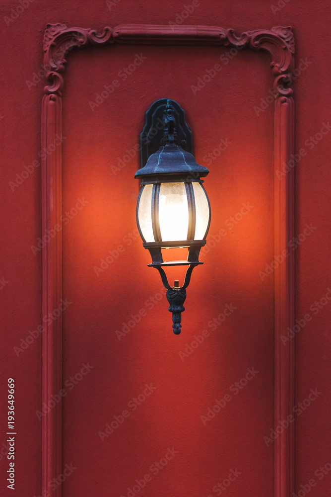Old vintage metal lantern on red facade of old building burning at night. Decoration ornament of house