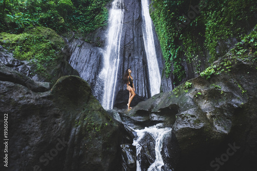 Woman enjoying near hidden in jungle cascade waterfall in Bali. Slim body and black swimsuit, fashion model. Dusun Kuning in Ubud area photo