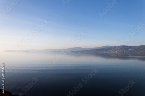Beautiful view of Trasimeno lake (Umbria, Italy), with hills and blue sky reflecting on water