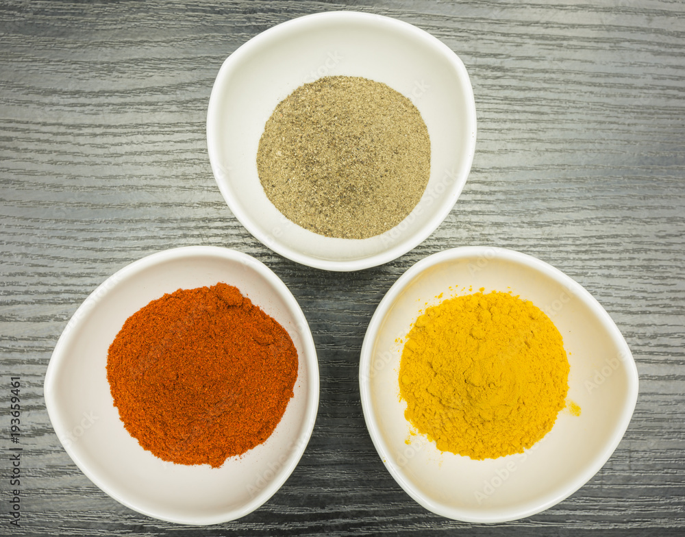 A set of three white bowls with spices - pepper, paprika and curry. View from above. A set of three white bowls with spices - pepper, paprika and curry. View from above.