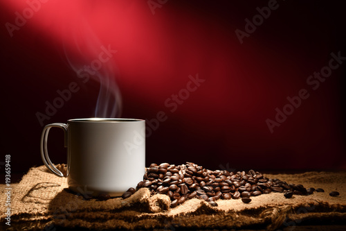 Cup of coffee with smoke and coffee beans on reddish brown background