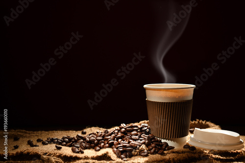 Paper cup of coffee with smoke and coffee beans on black background
