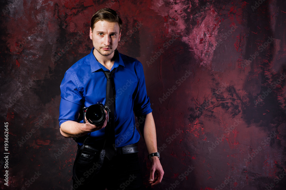 Studio portrait of stylish professional photographer man with camera, wear on blue shirt and necktie.