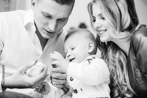 father holds a little yellow chicken and a little boy and his mom look at him and smile on a black and white photo