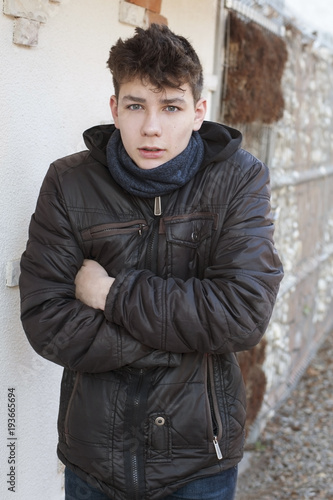 A beautiful male teenager standing on the street and embracing himself. He shows that he is cold