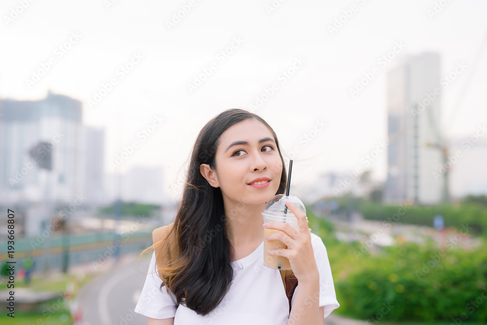 Young beautiful girl standing on a bridge with city view with coffee cup in her hand. Young beautiful girl standing on a bridge with city view with coffee cup in her hand.