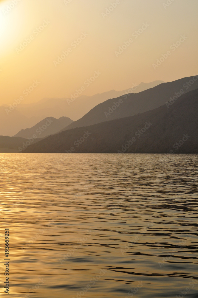 sunset on the coast of the Gulf of Oman against the backdrop of mountain ranges and the orange sky