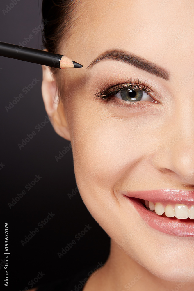 Smiling woman painting eyebrows with black pencil