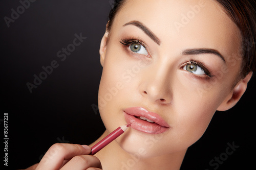 Woman drawing contour on lips with red pencil