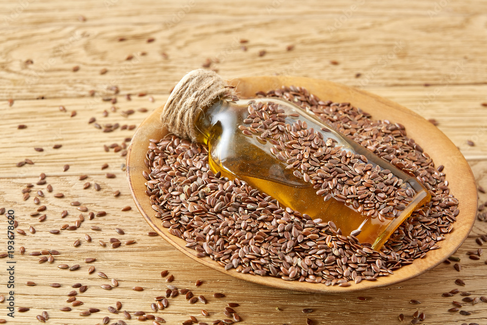 Top view closeup picture flax seeds and linseed oil in a glass bottle on a wooden background, shallow depth of field. Top view closeup picture flax seeds and linseed oil in a glass bottle on a wooden background, shallow depth of field.