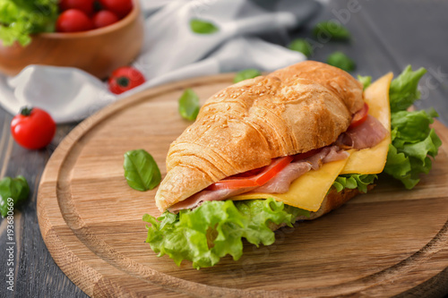 Wooden board with delicious croissant sandwich on table