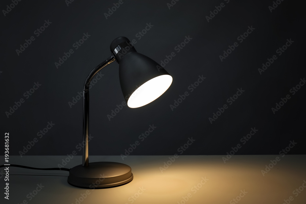 Stylish desk lamp on table in darkness Stylish desk lamp on table in darkness