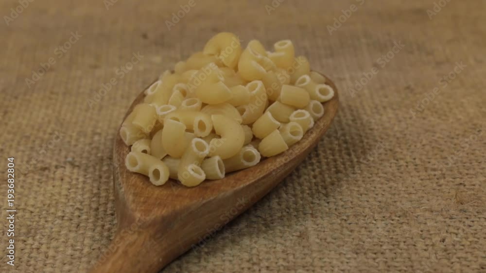 Close-up, spoon rotation with a pile of macaroni lying on burlap. Close-up, spoon rotation with a pile of macaroni lying on burlap.