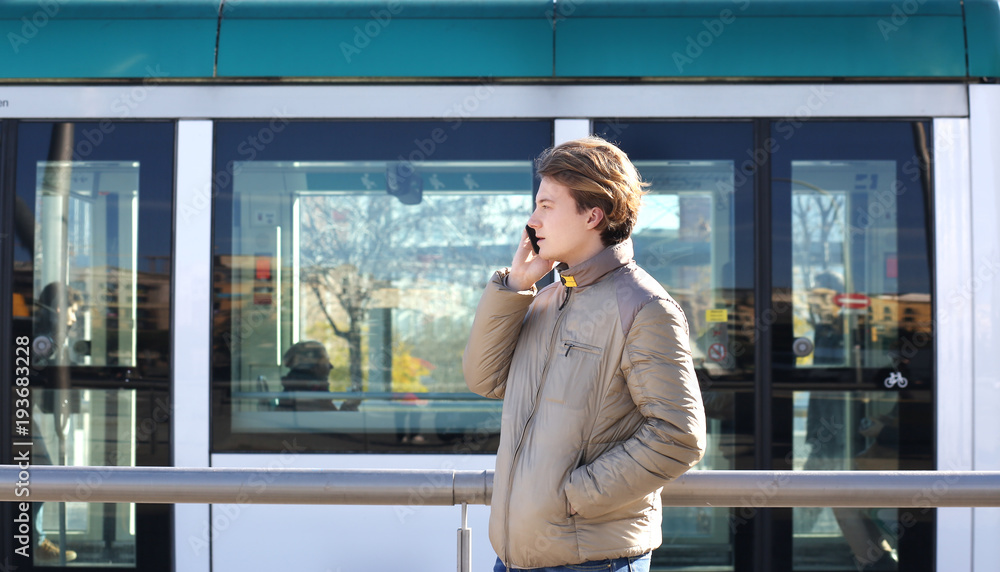Teenage boy typing text message.Using smart phone.Tram station