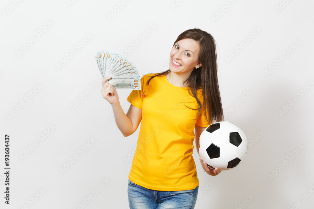 European young fun woman, football fan or player in yellow uniform holding bunch of money banknotes, soccer ball isolated on white background. Sport, play football game, excitement lifestyle concept. European young fun woman, football fan or player in yellow uniform holding bunch of money banknotes, soccer ball isolated on white background. Sport, play football game, excitement lifestyle concept.