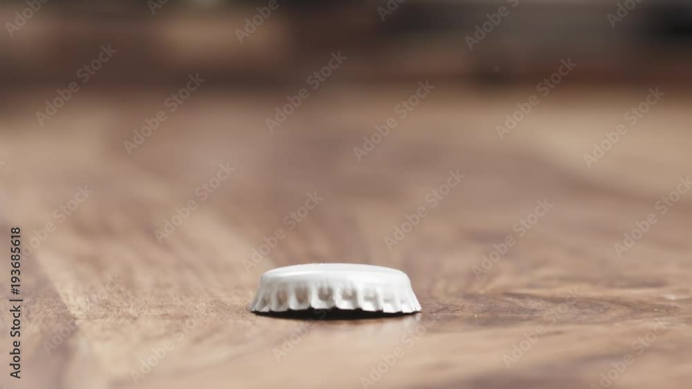 Slow motion closeup of bottle cap falling on wood table Slow motion closeup of bottle cap falling on wood table