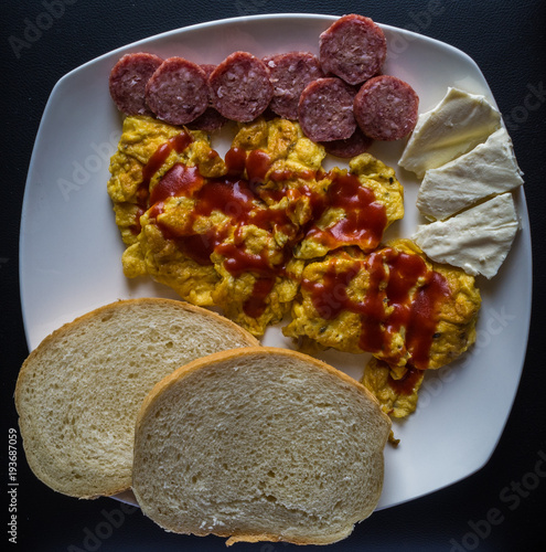 Scrambled eggs with ketchup with bread, salami  and cheese