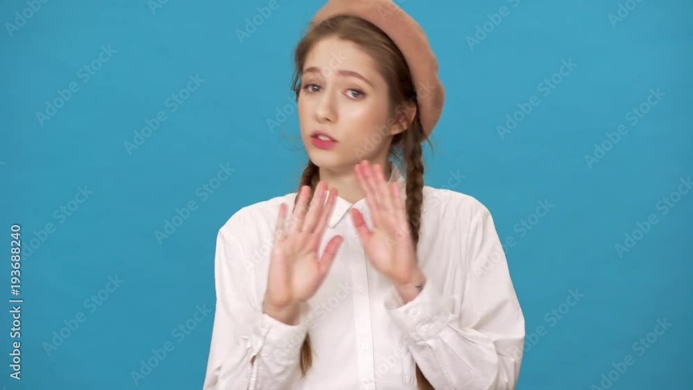 Portrait closeup of persistent woman 20s wearing french beret shaking head and waving hands in denial or disagreement, isolated over blue background Portrait closeup of persistent woman 20s wearing french beret shaking head and waving hands in denial or disagreement, isolated over blue background