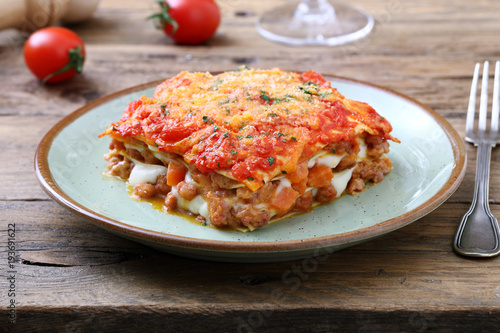 lasagna tradizionale italiana con salsa bolognese e parmigiano su sfondo rustico