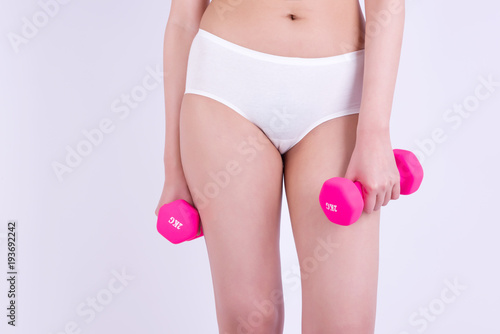 Body in good shape. Young woman holding dumbbell in her hand